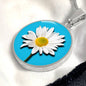 Daisy Birth Flower April Graphic Epoxy Disc Necklace. Clear shiny epoxy shows a white petal flower with yellow canter on a light blue background. The jewellery is made of high quality surgical steel or with an 18k gold finish option with an option to engrave a short love you message or special date. Luxury Necklace: 18-22" (45-56cm) adjustable
Circle Pendant: 0.9” x 0.9” (23.5mm x 23.5mm)